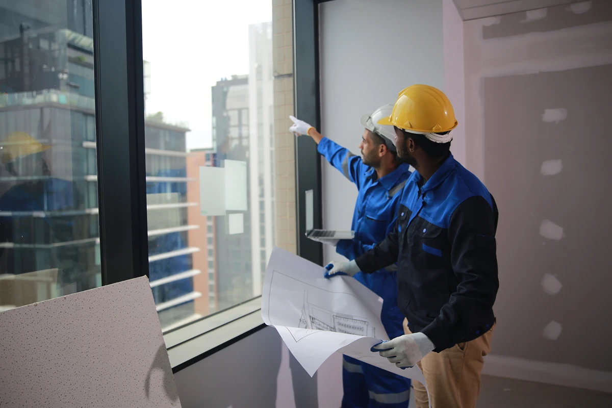 Two workers in a renovated room discussing change of use, one pointing at window, both wearing hard hats